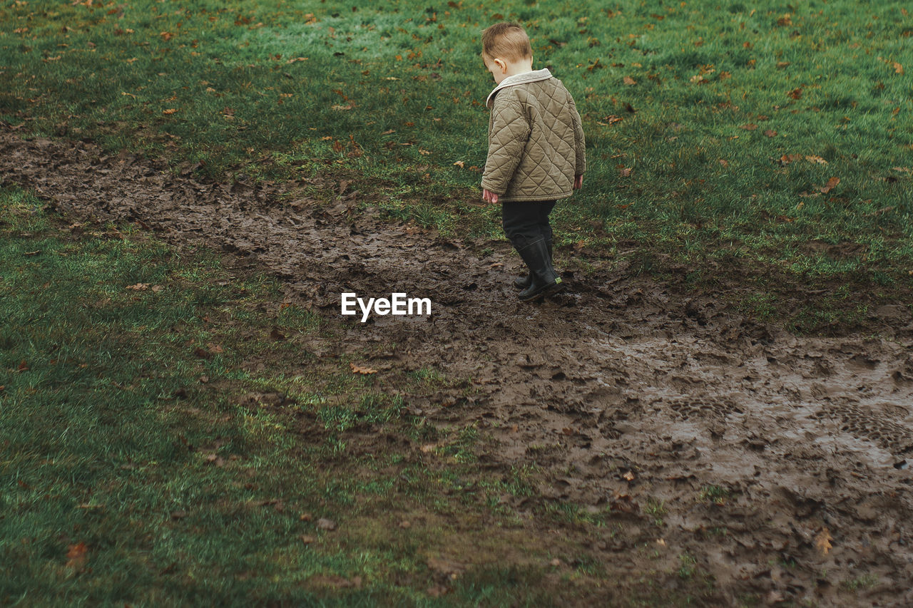 REAR VIEW OF CHILD WALKING ON FIELD