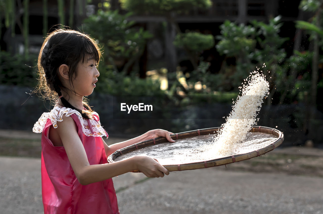 Side view of girl cleaning rice on wicker container