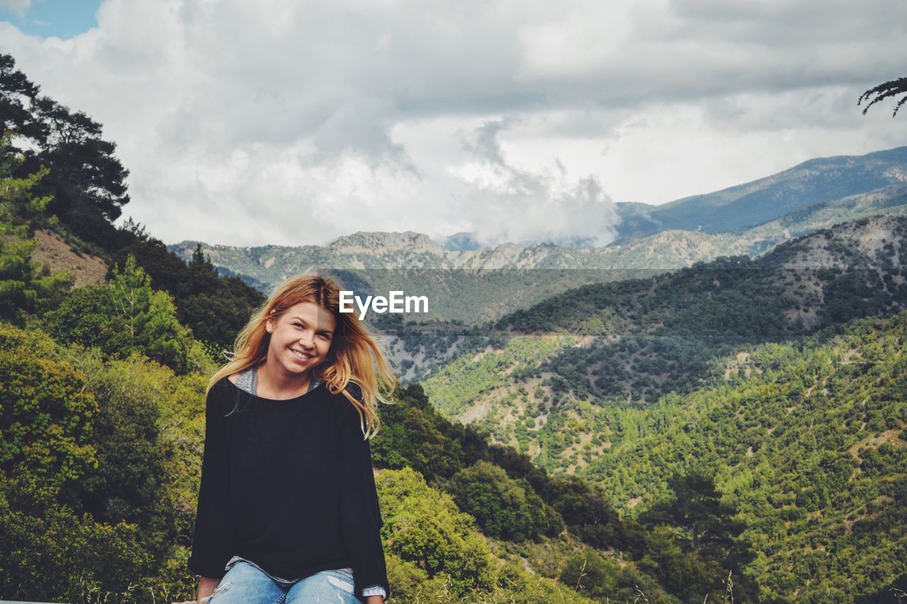 Portrait of smiling young woman sitting against mountain ranges