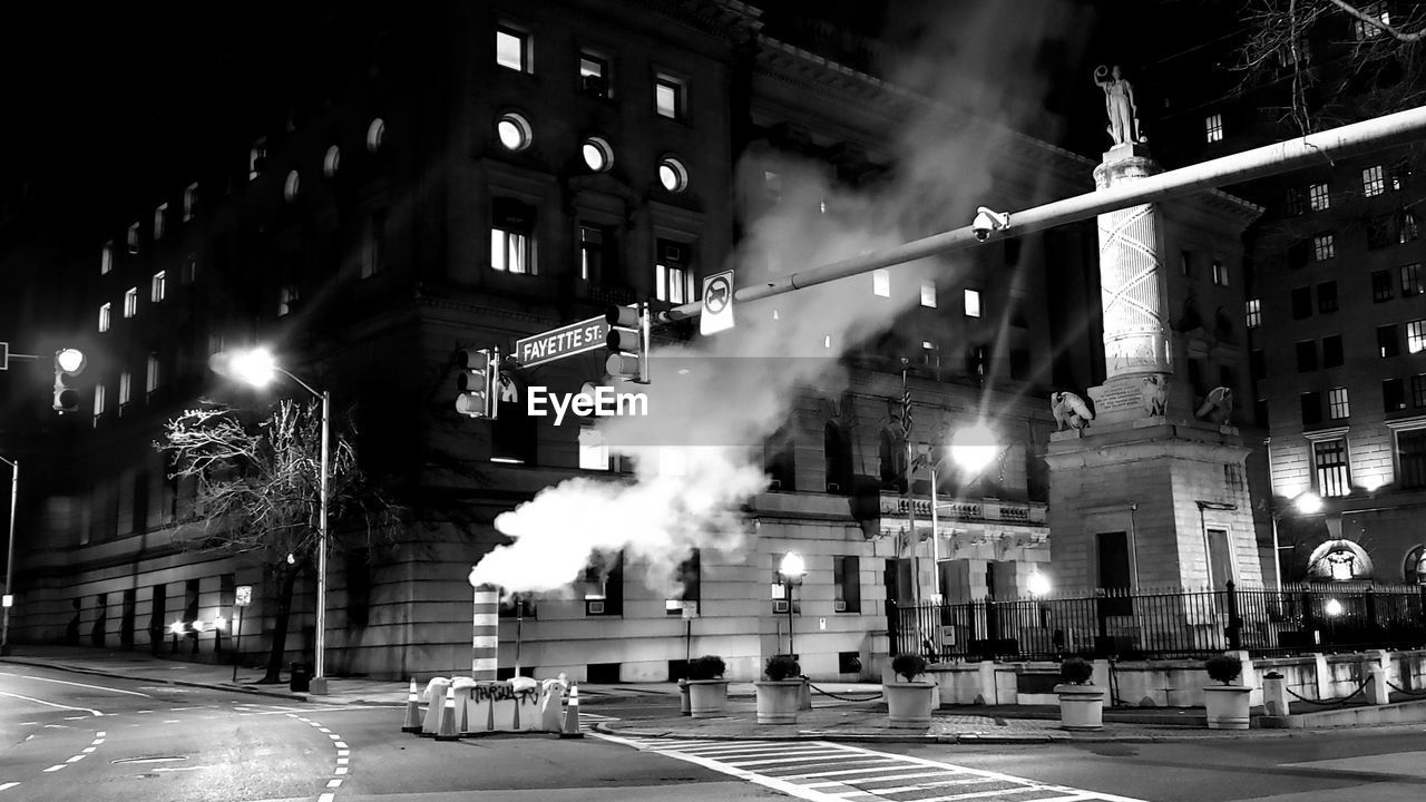CARS ON CITY STREET BY BUILDINGS AT NIGHT