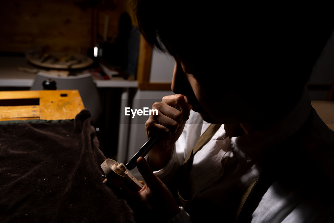 Young chinese female violin maker working with gouge to making a new violin in her workshop