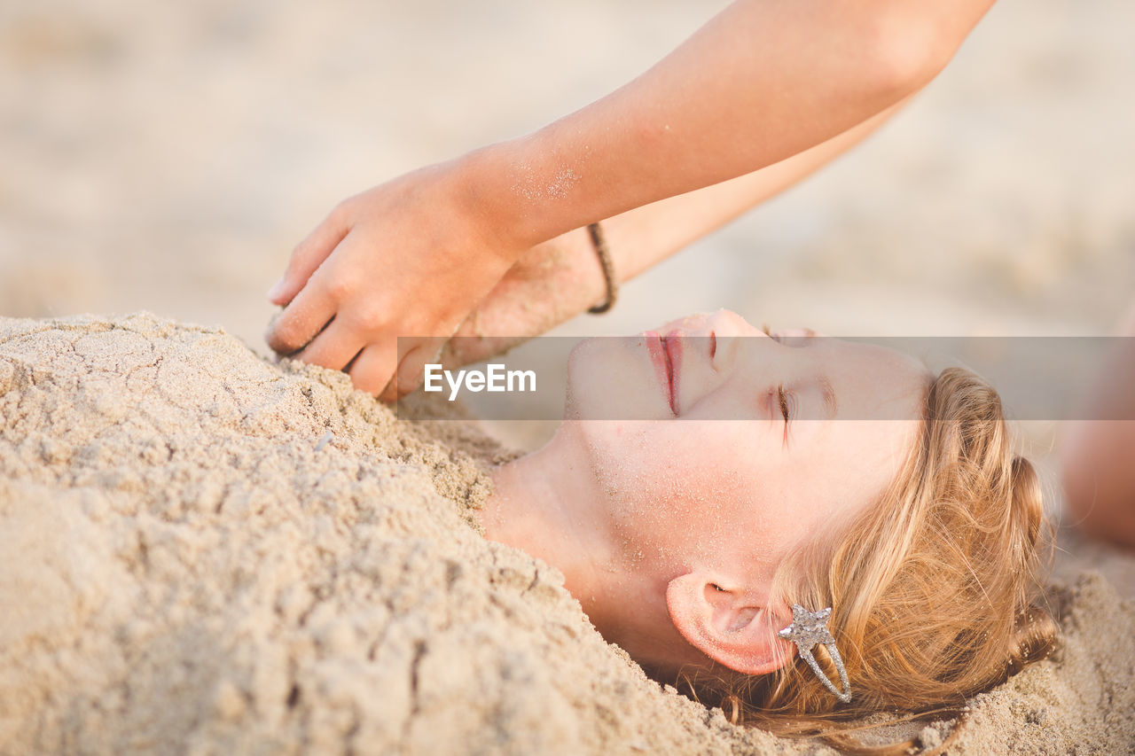 Cropped hands of girl buried sister in sand