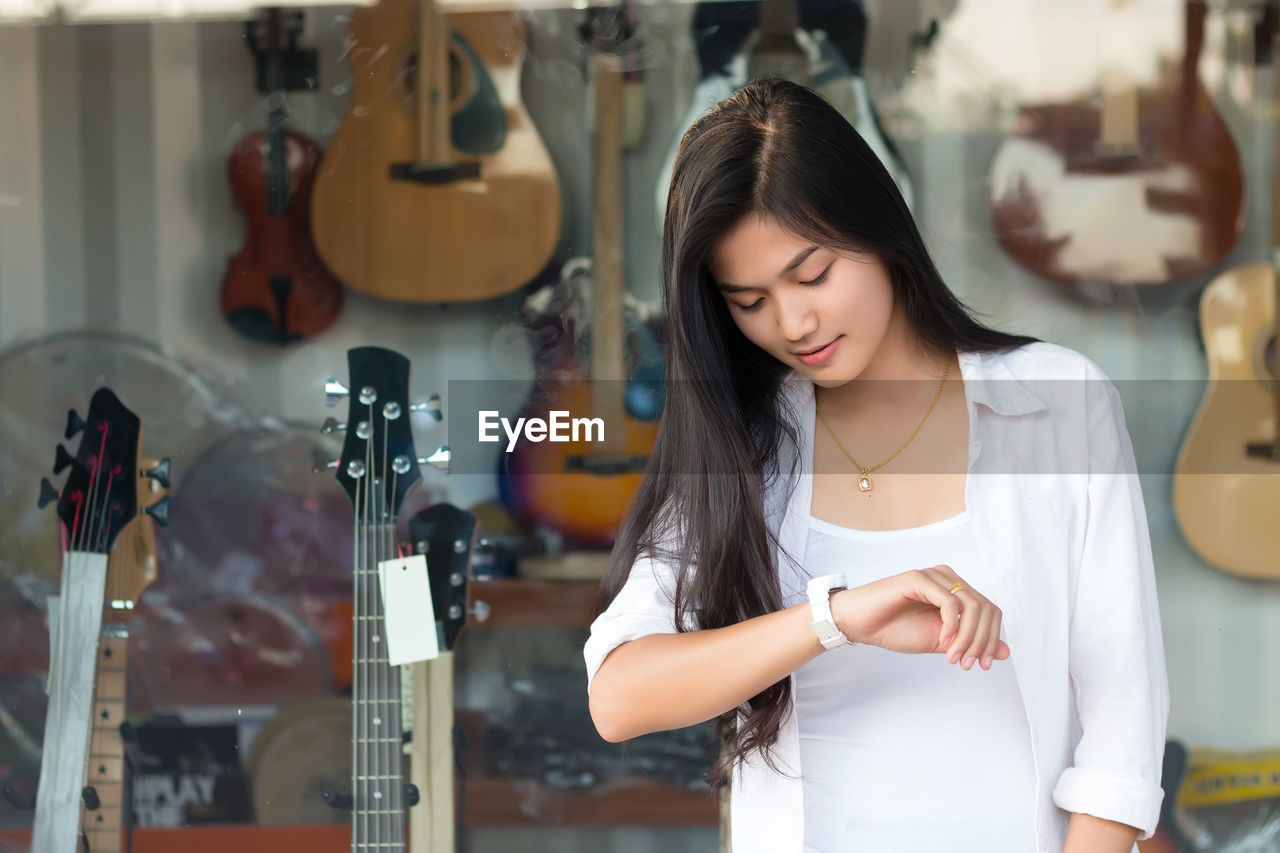 Young woman checking time while standing against guitar store