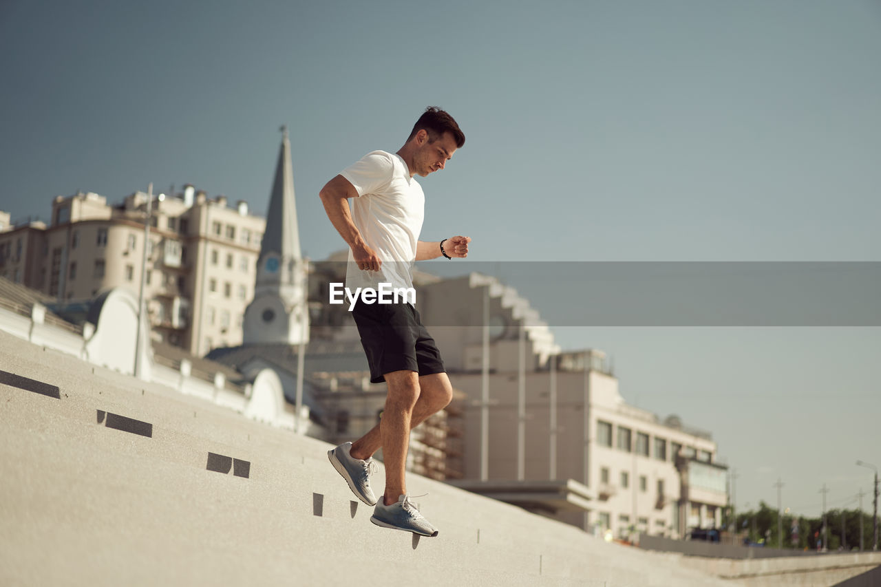 Side view of athletic male running downstairs while training on sunny day in city in summer