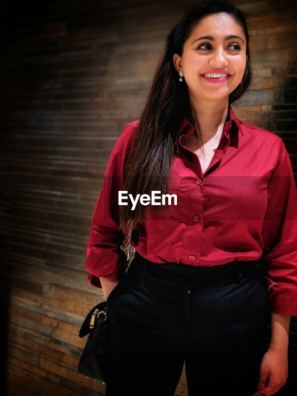 PORTRAIT OF A SMILING YOUNG WOMAN STANDING AGAINST WALL