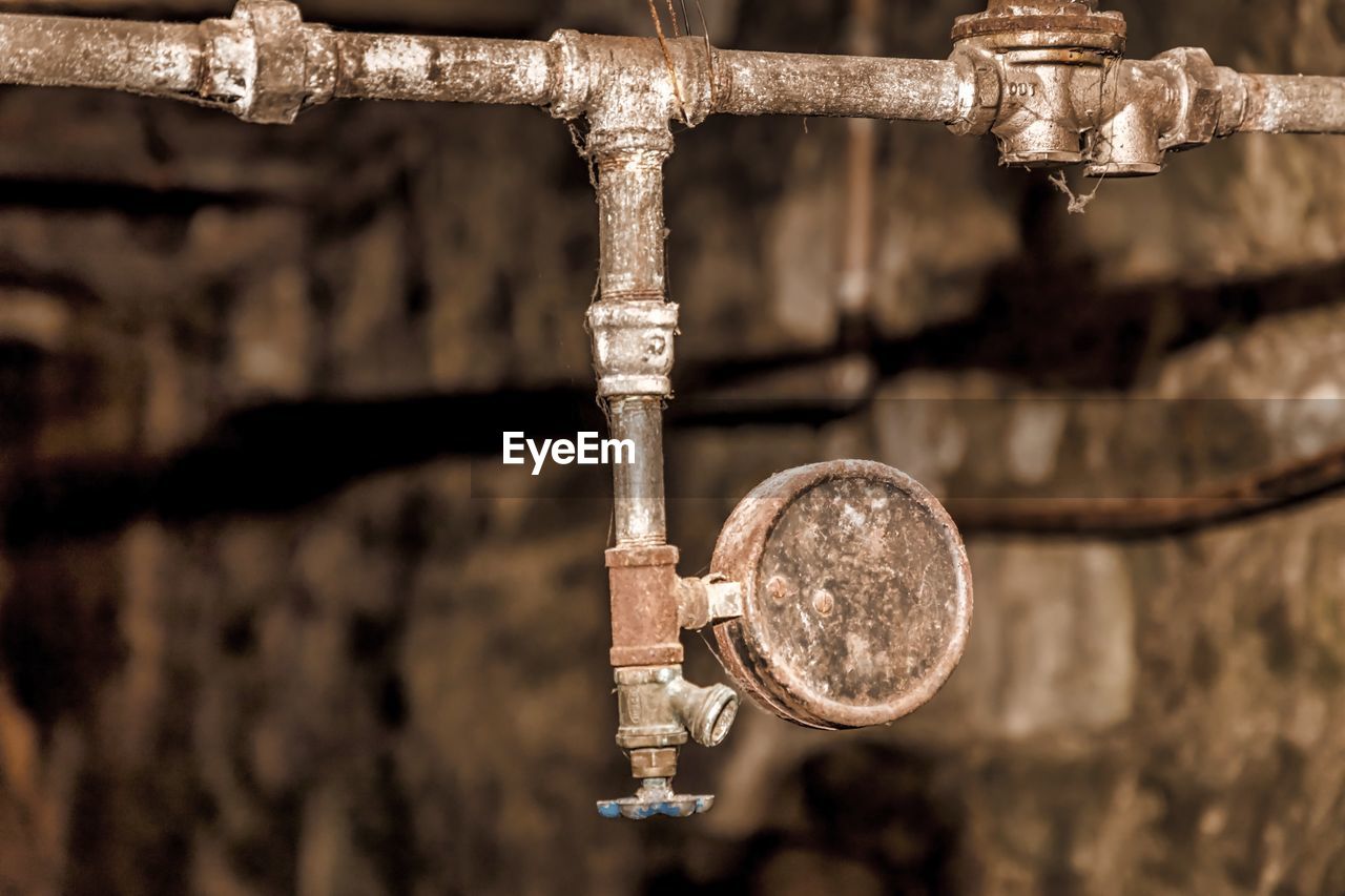 Close-up of rusty metallic pipe and pressure gauge at abandoned factory