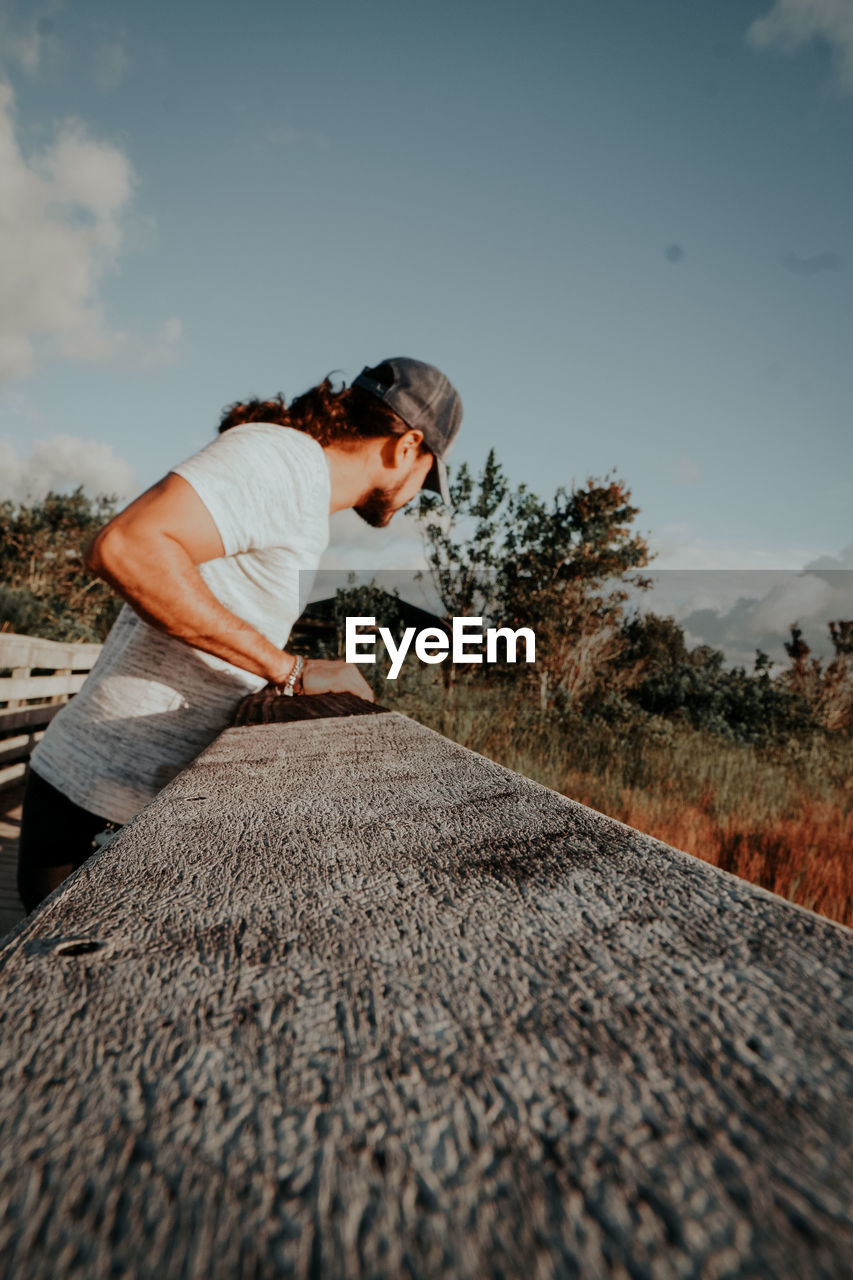 MAN STANDING ON RAILROAD TRACK AMIDST FIELD AGAINST SKY