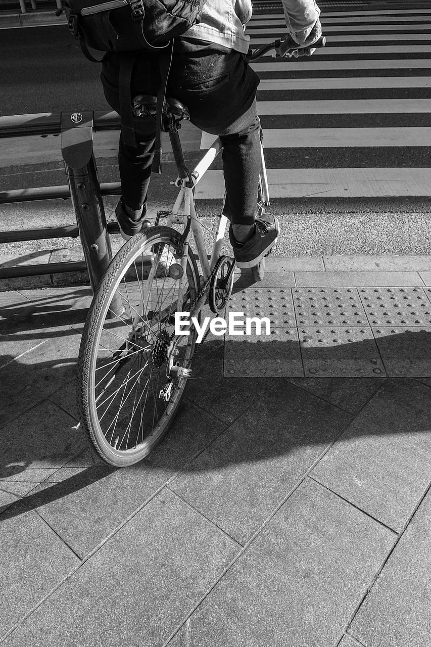 REAR VIEW OF MAN RIDING BICYCLE ON ROAD