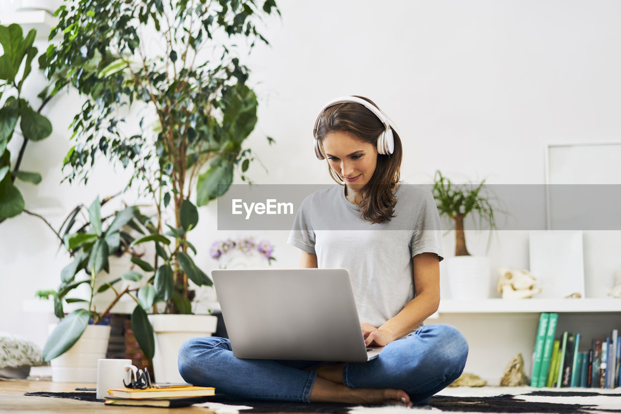 Young woman at home sitting on the floor using laptop and listening to music