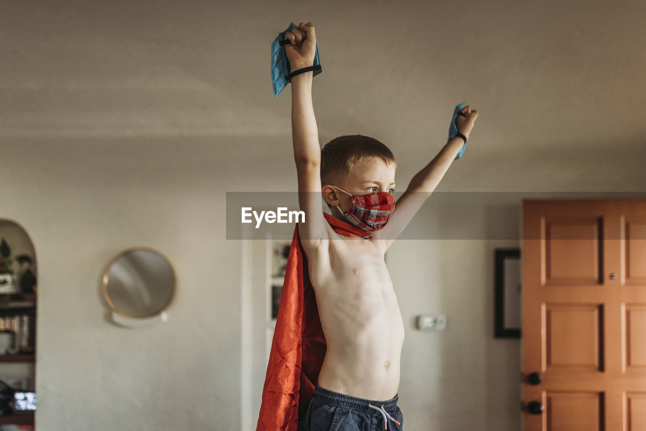 Young boy with arms outstretched wearing superhero costume and mask