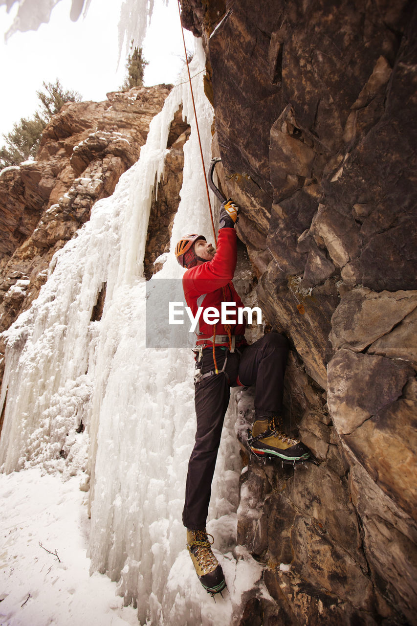 Full length of hiker climbing frozen waterfall