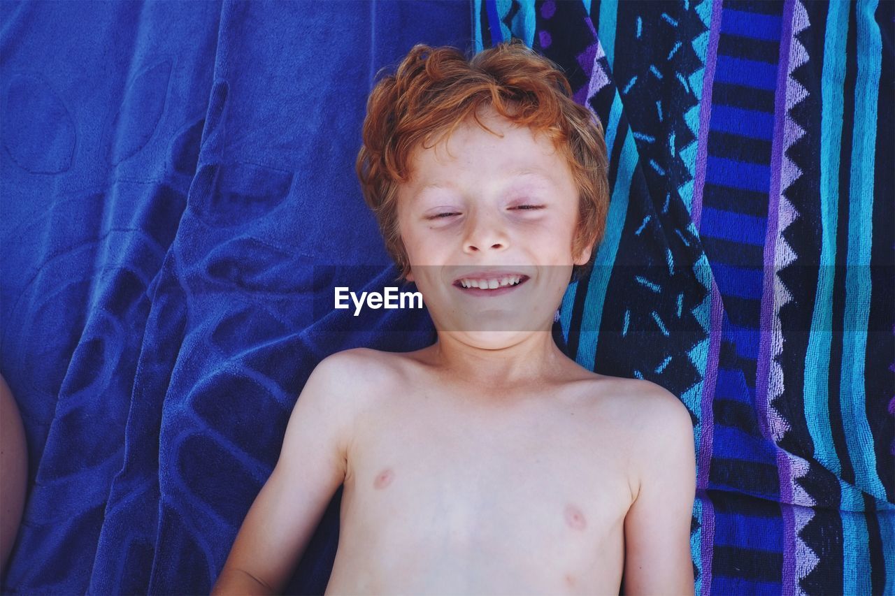 High angle view of smiling shirtless boy lying at home