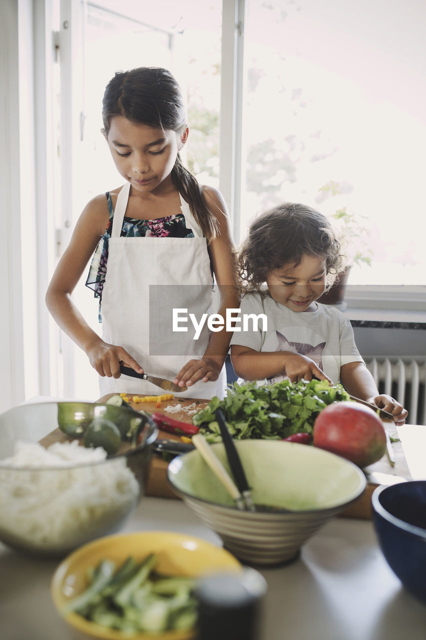 Sisters chopping vegetables while preparing food at table