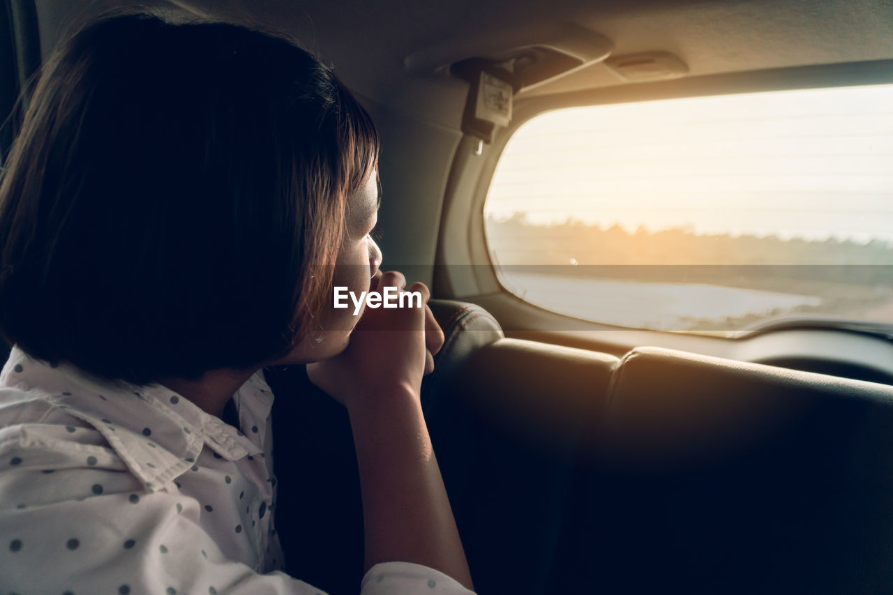 Girl looking through window while sitting in car