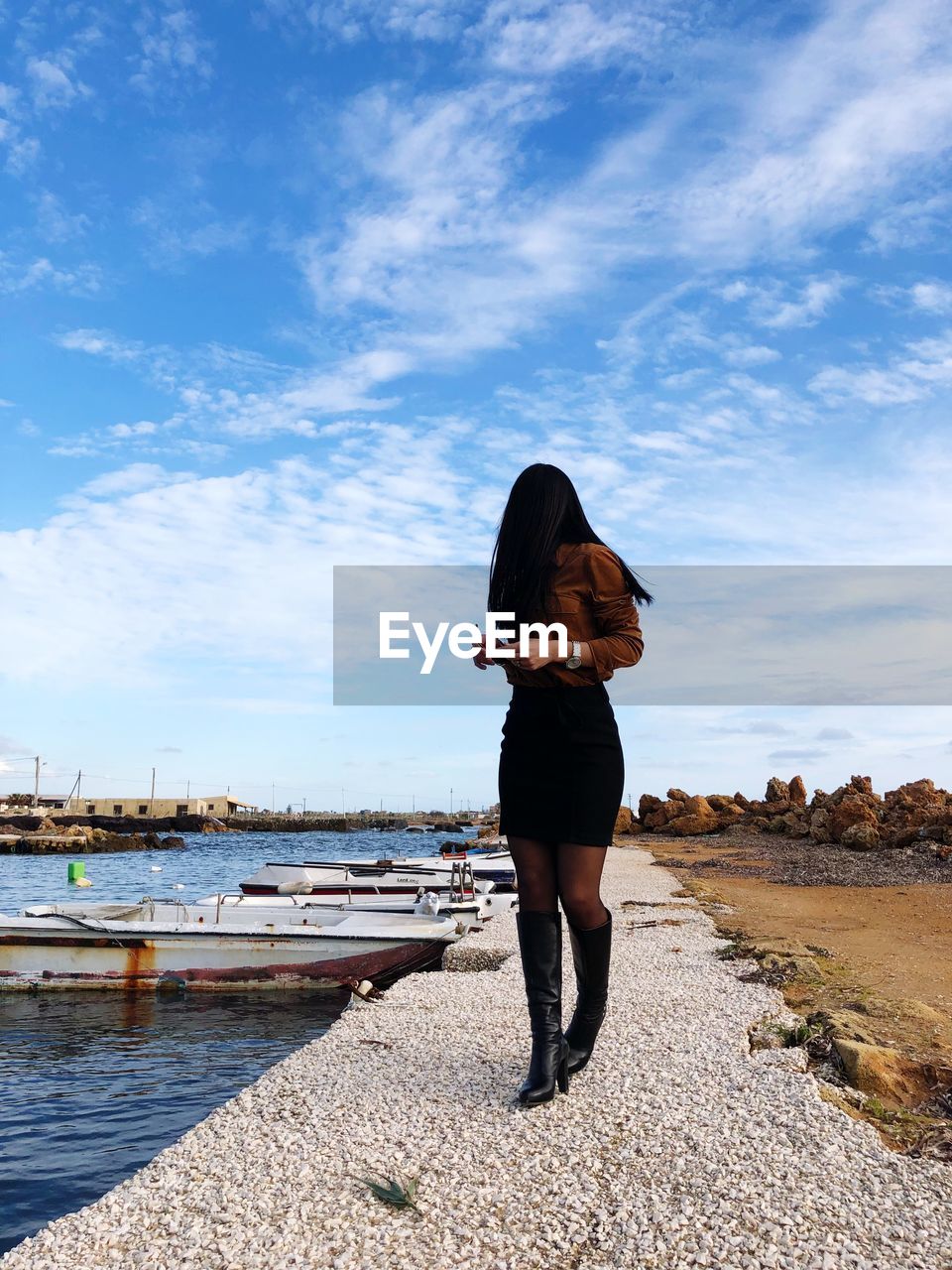 Young woman standing at shore against cloudy sky