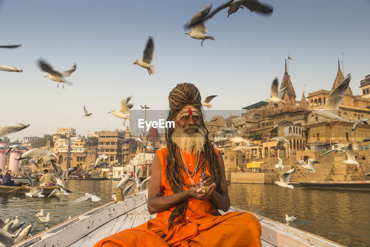 Birds flying over sadhu on boat in sea against sky