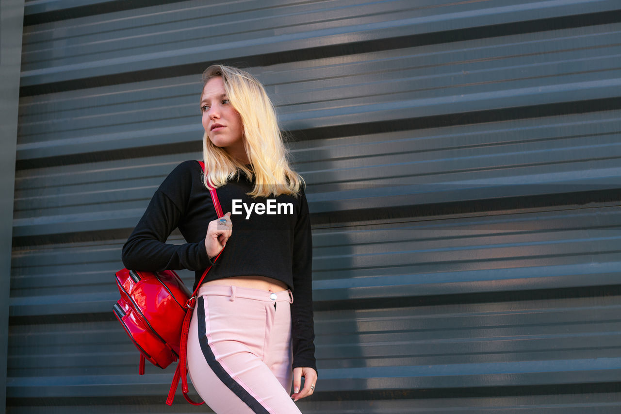 Young blond hair woman carrying a backpack. blond hair girl walking on the street with backpack.