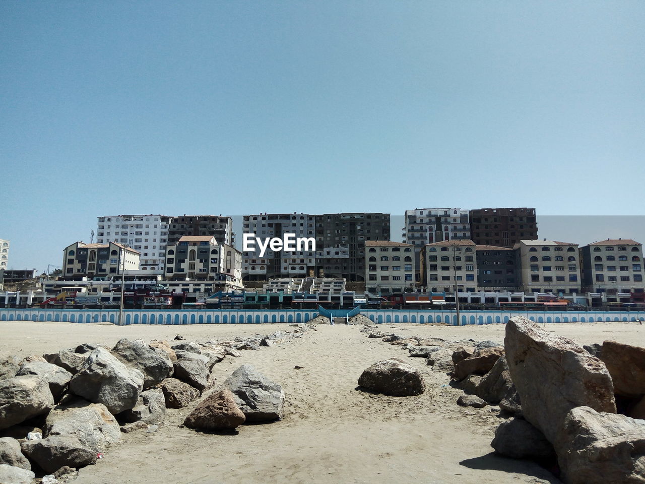 Rocks at sandy beach by buildings against clear sky