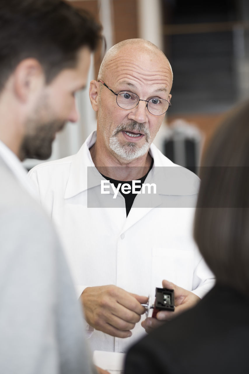 Mature engineer explaining machine part to business people in factory