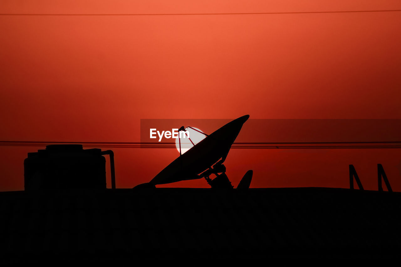 Silhouette satellite dish on building terrace against orange sky