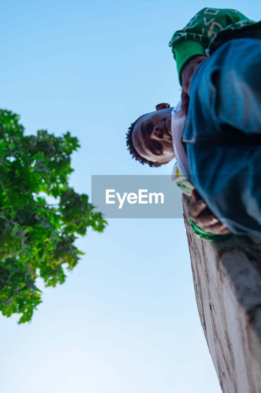 LOW ANGLE VIEW OF MAN ON TREE AGAINST CLEAR SKY