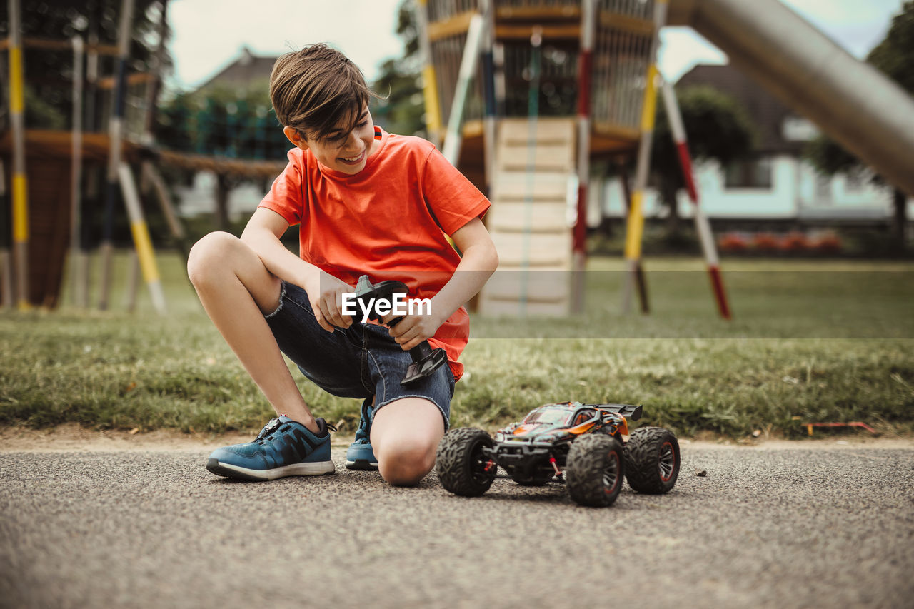 Teen boy with electric remote control car toy play outdoor on sidewalk and have fun while enjoy