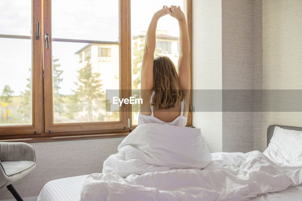 rear view of young woman sitting on bed at home