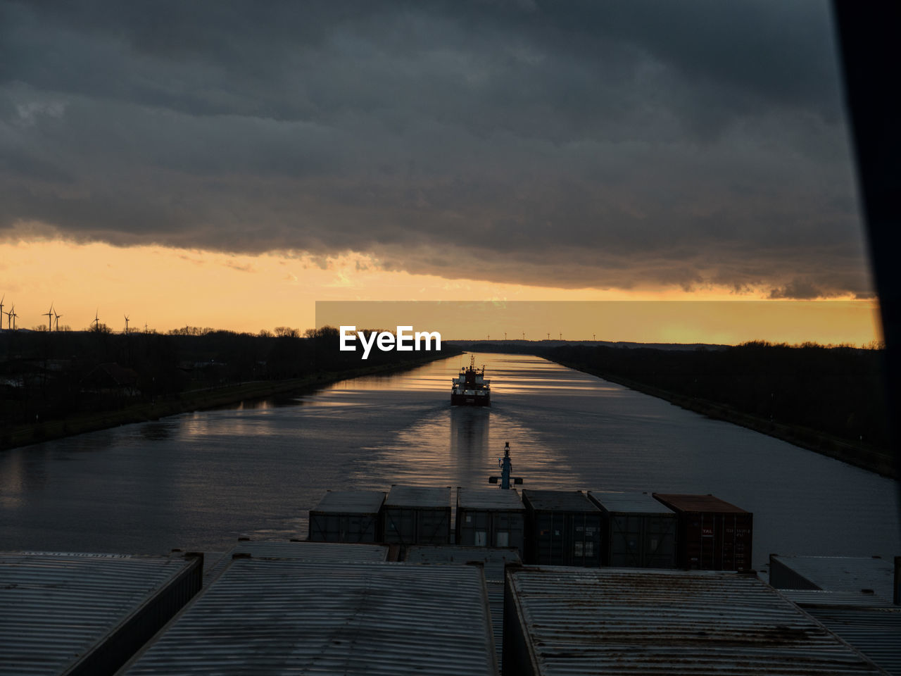 Container ship in kiel canal against cloudy sky during sunset