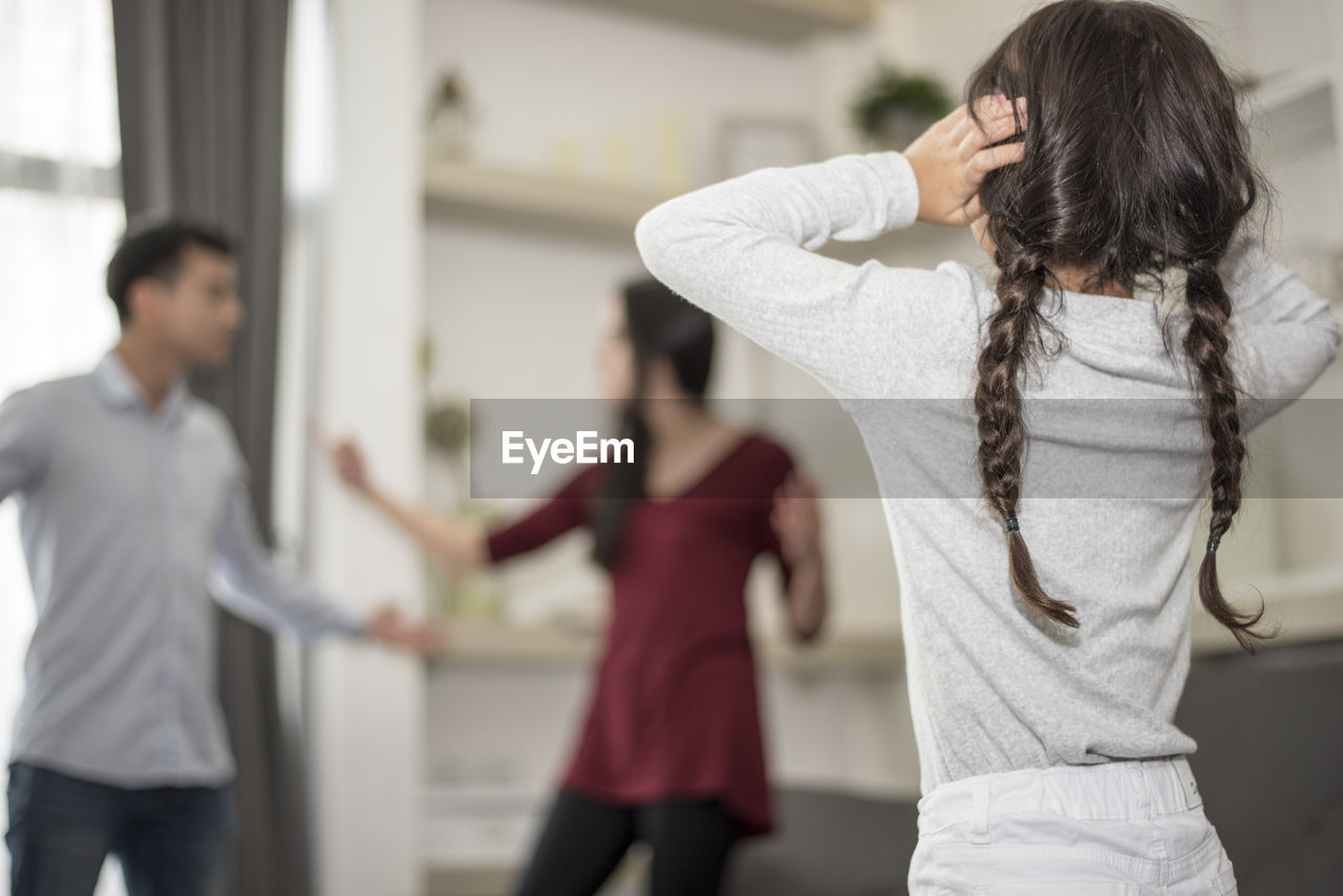 Girl covering ears while parents arguing at home