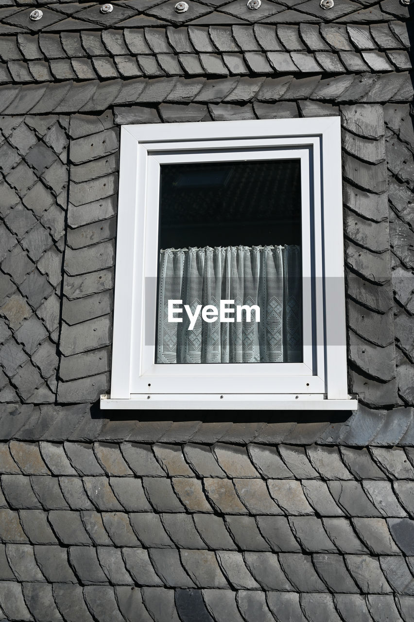 Gray slate wall siding on a house with a white window