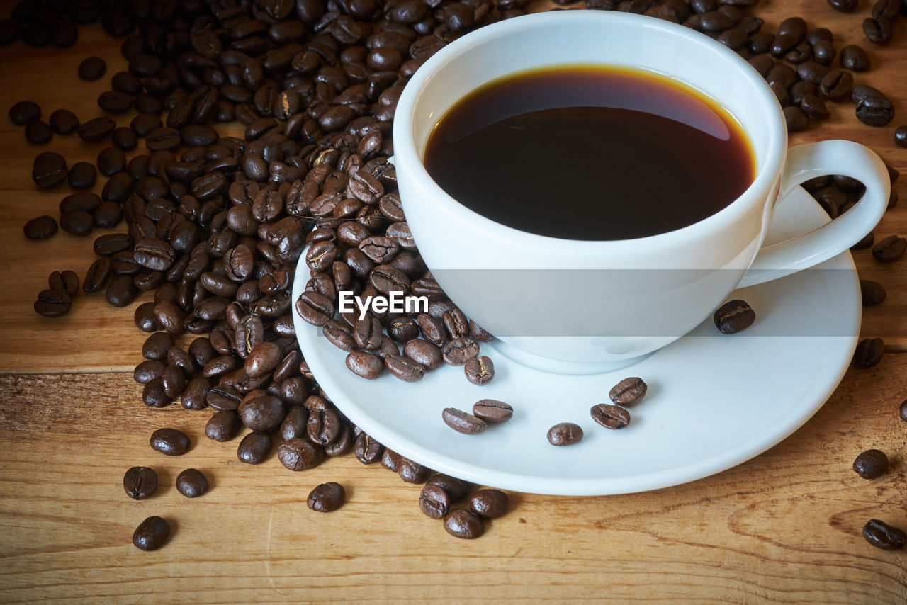 High angle view of black coffee with roasted beans on table