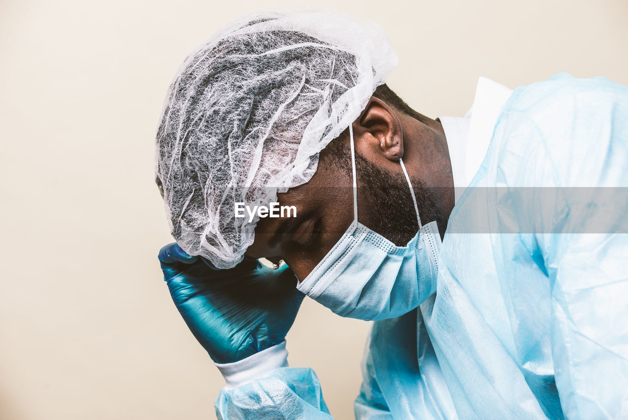 Doctor wearing mask sitting against colored background