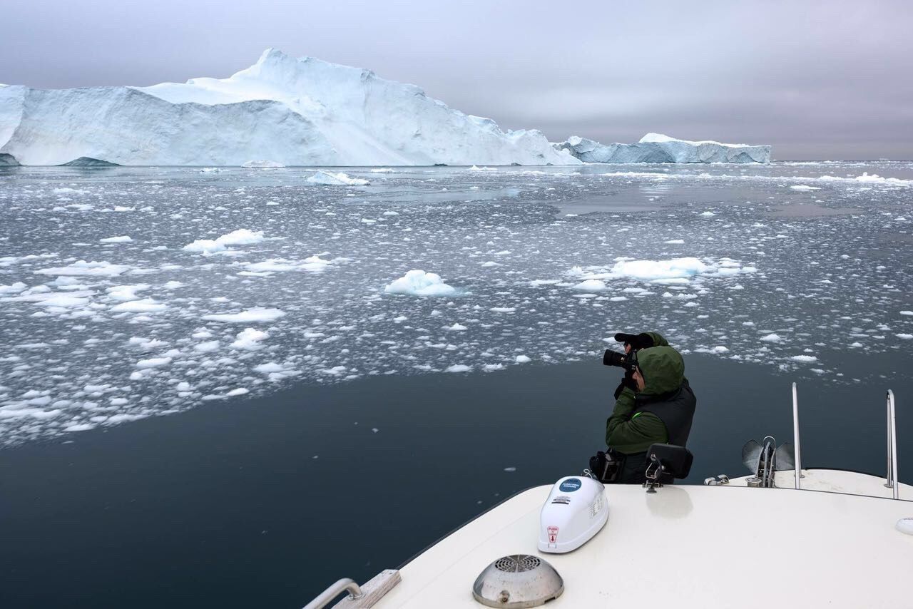 Mature man photographing while standing on boat against cloudy sky during winter