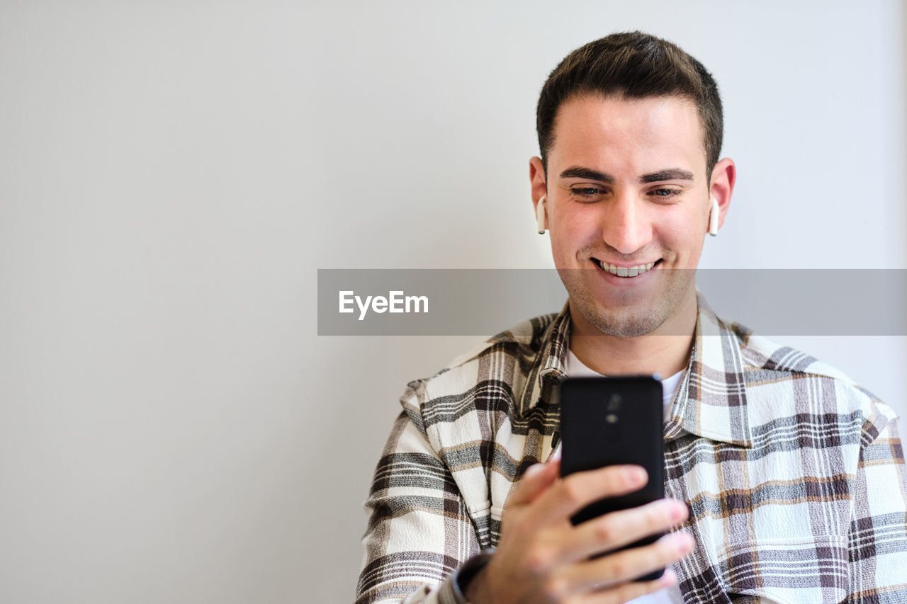 Young man with earphones smiling and looking at smartphone. chilling at home. copy space.