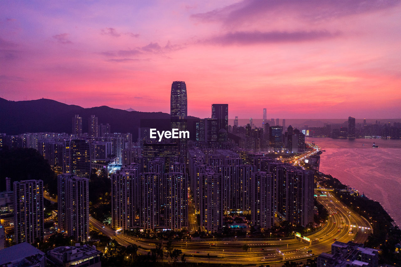 Illuminated city buildings against sky during sunset