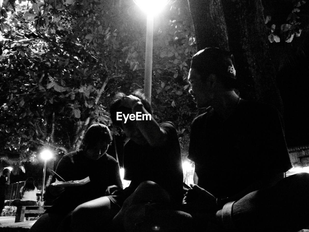 Friends sitting against trees at night