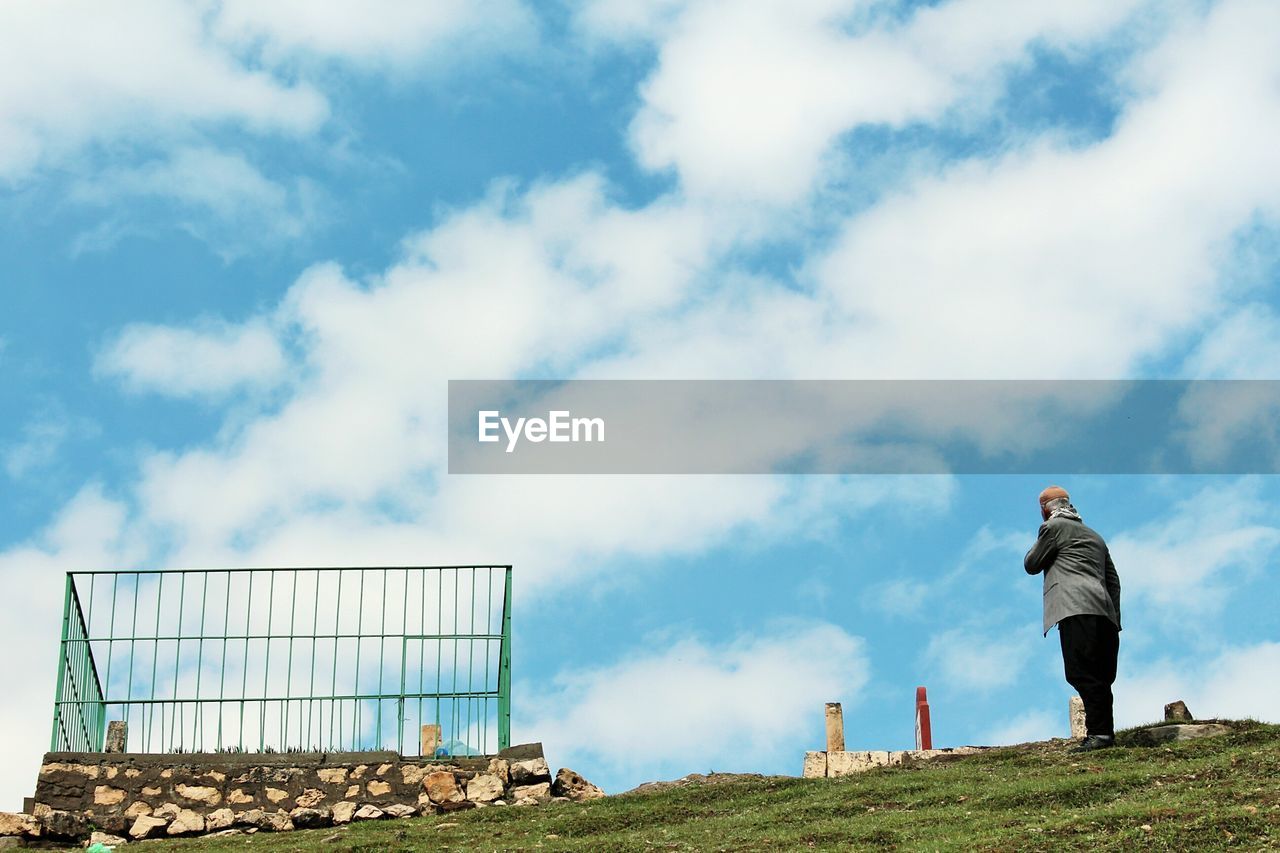 Low angle view of person standing on hill against cloudy sky during sunny day