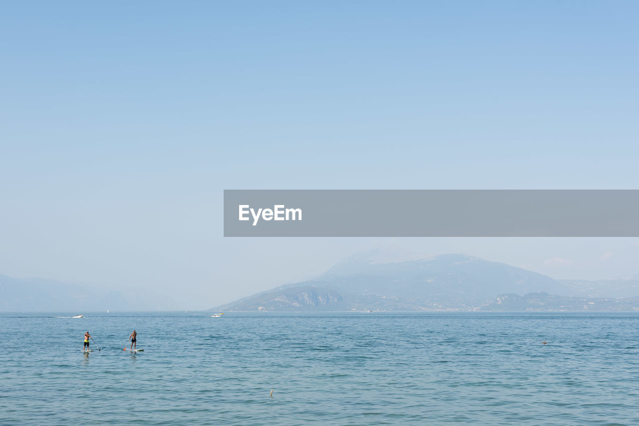 Friends paddleboarding in sea against clear sky