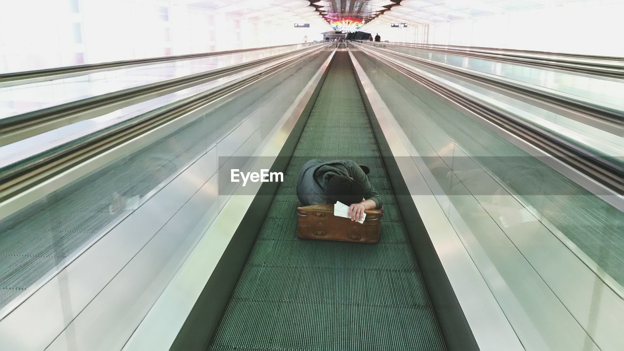 Man sleeping on suitcase on moving walkway