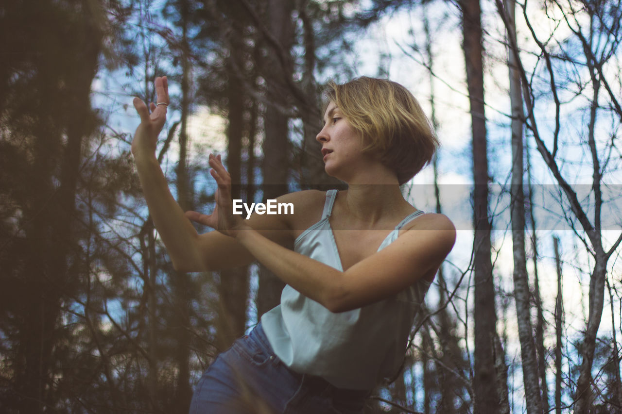 Low angle view of young woman dancing in forest