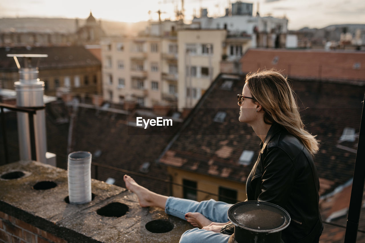 Woman wearing sunglasses while sitting on retaining wall in city