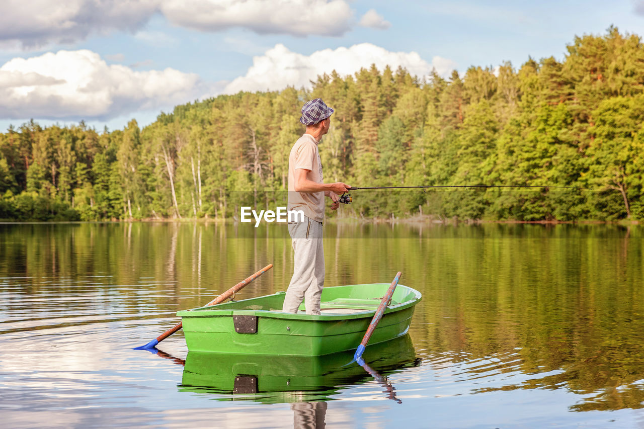 water, lake, tree, nature, one person, adult, reflection, plant, nautical vessel, transportation, full length, leisure activity, holiday, boating, vacation, men, trip, day, activity, sky, standing, vehicle, forest, travel, boat, tranquility, canoe, beauty in nature, paddle, oar, cloud, lifestyles, summer, outdoors, mode of transportation, clothing, tranquil scene, scenics - nature, adventure, side view, person, weekend activities, travel destinations, casual clothing, green, hat, environment, sports, holding, fishing, mature adult, relaxation, young adult, women, sunlight, recreation