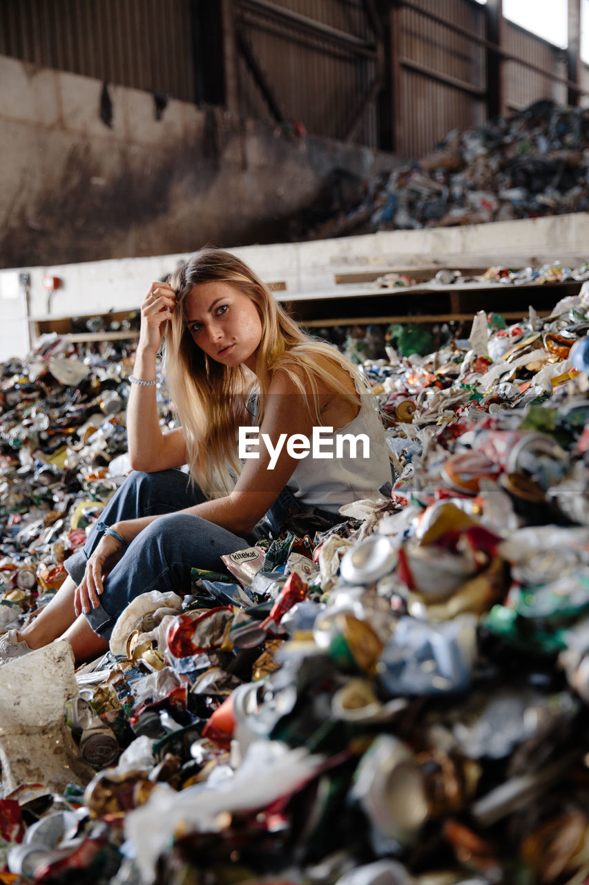 PORTRAIT OF BEAUTIFUL YOUNG WOMAN SITTING ON GARBAGE AT PARK