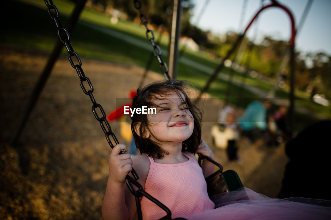 Young girl on swing, closing eyes and smiling