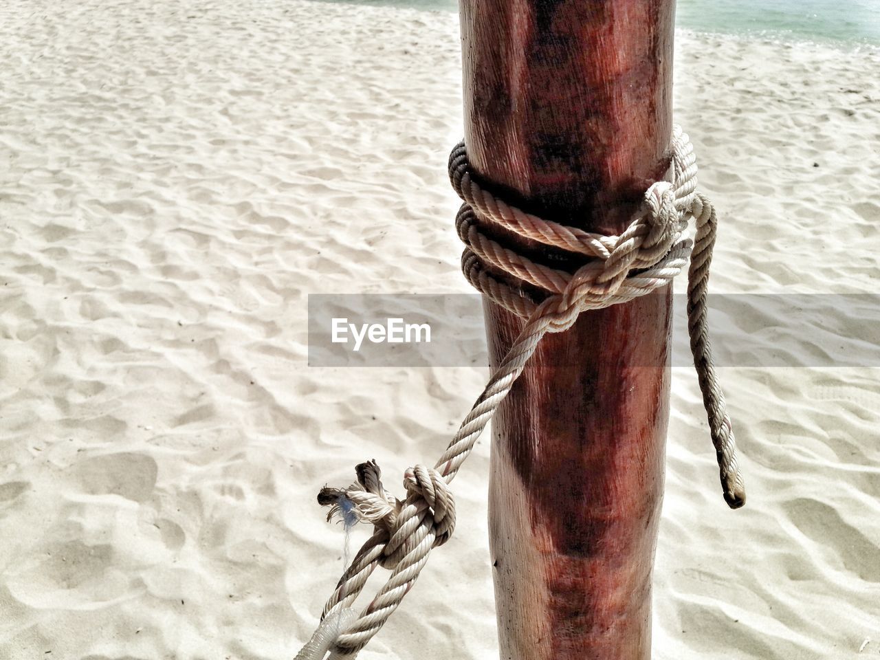 Close-up of rope tied on wooden post at sandy beach