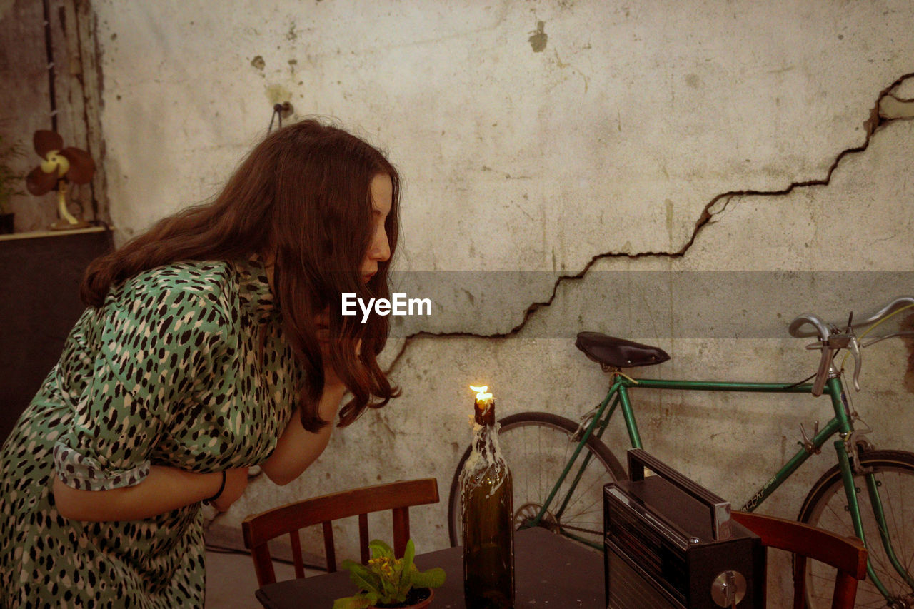 WOMAN SITTING ON TABLE AGAINST WALL AT HOME