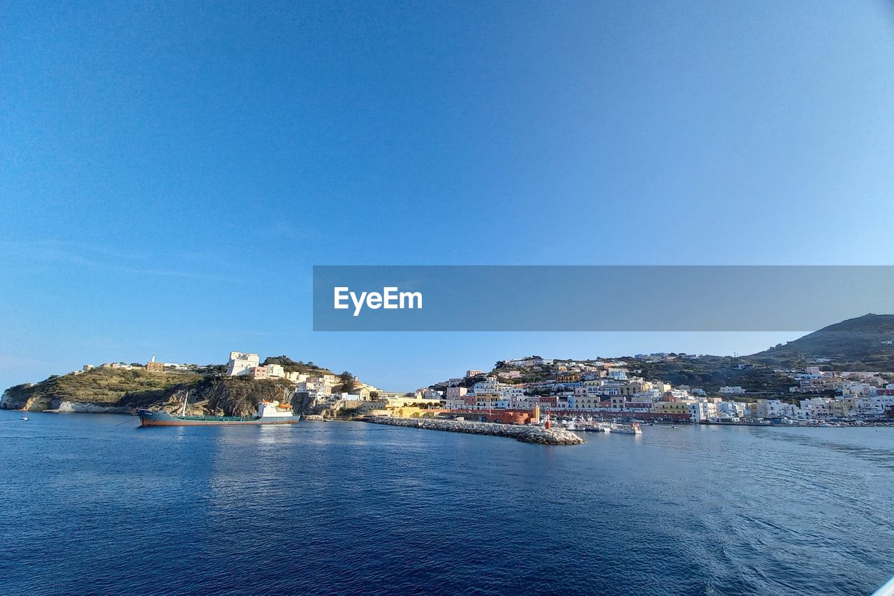 VIEW OF TOWNSCAPE BY SEA AGAINST CLEAR SKY