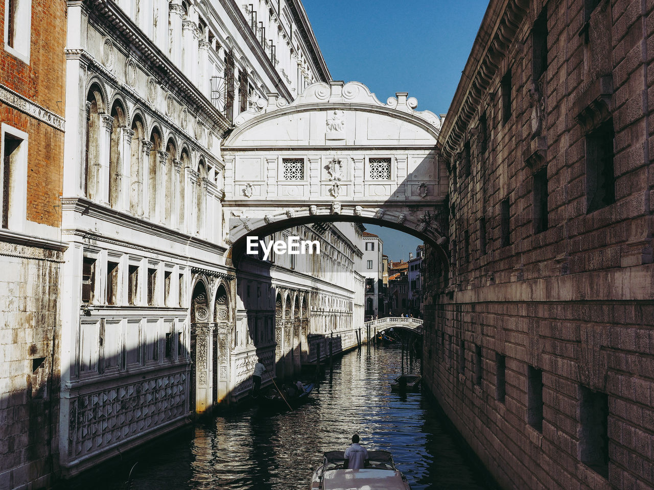 Canal amidst buildings against blue sky in city during sunny day