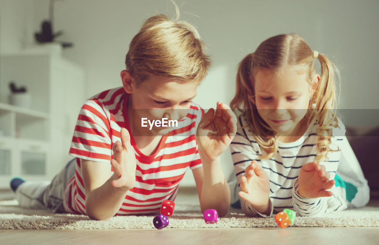 Cute sibling playing with dice on floor at home