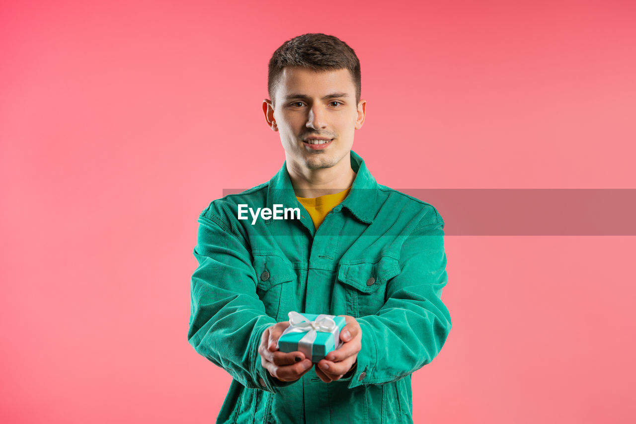 one person, portrait, studio shot, colored background, looking at camera, adult, young adult, indoors, waist up, front view, men, standing, clothing, smiling, copy space, pink background, person, emotion, outerwear, happiness, brown hair, holding, casual clothing, beard, facial hair